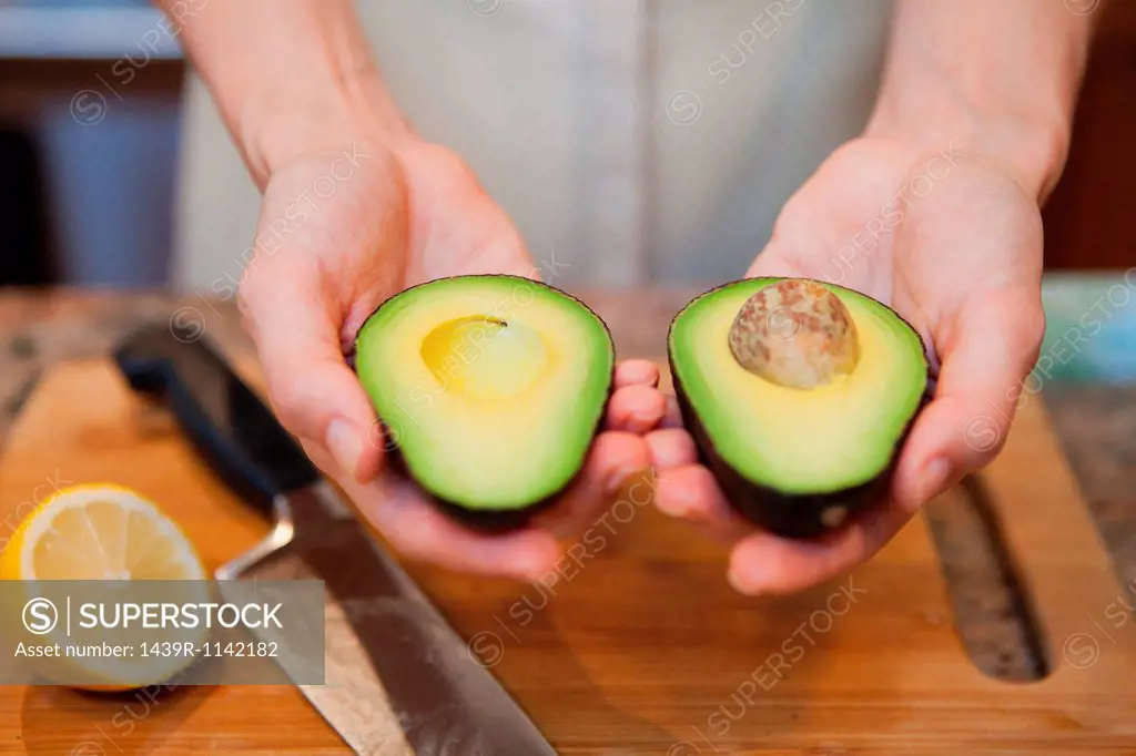 Mid adult woman holding sliced avocado
