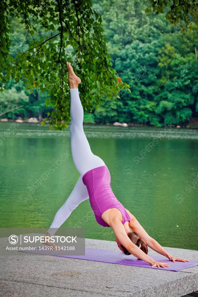 Mid adult woman performing yoga downward dog split pose by river