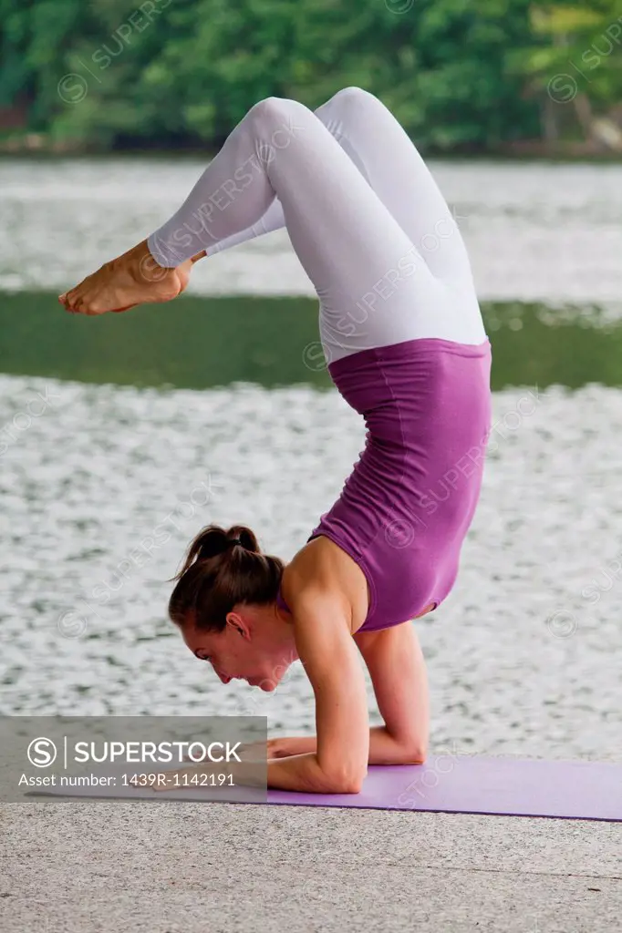 Mid adult woman performing yoga scorpion pose by river, looking away