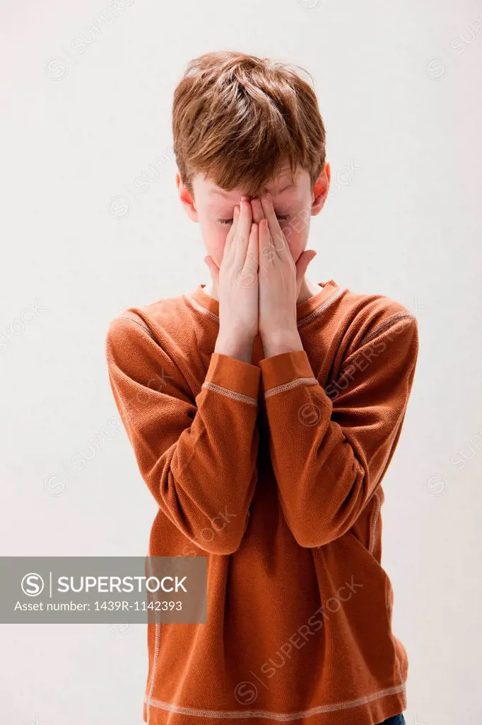 Boy in brown sweater rubbing eyes, studio shot