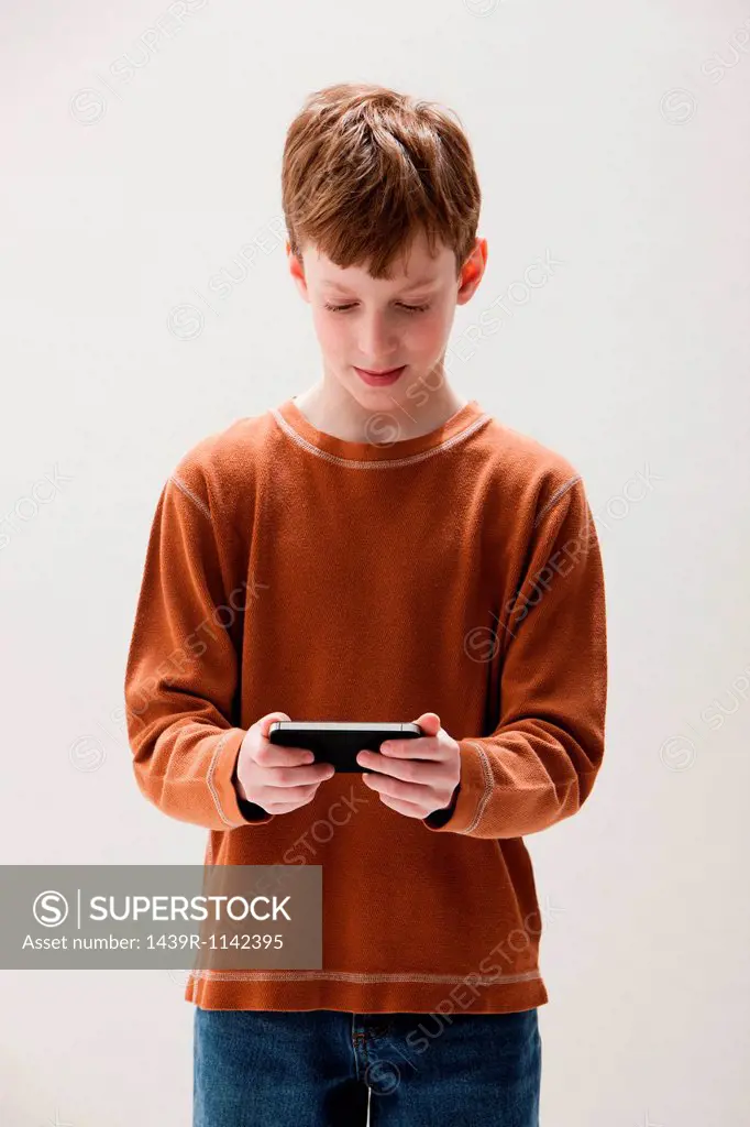 Boy in brown sweater playing hand held video game, studio shot