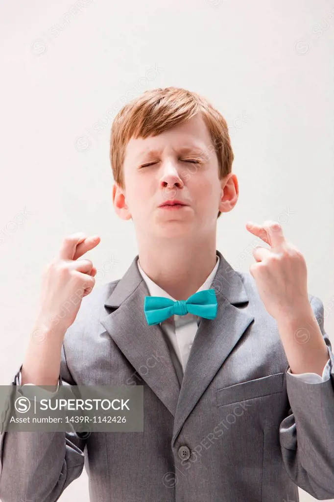 Boy wearing grey suit with fingers crossed, studio shot