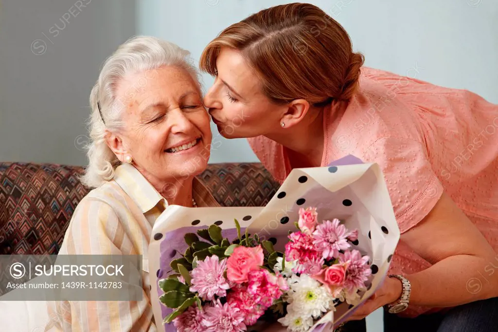 Daughter giving senior mother bouquet of flowers