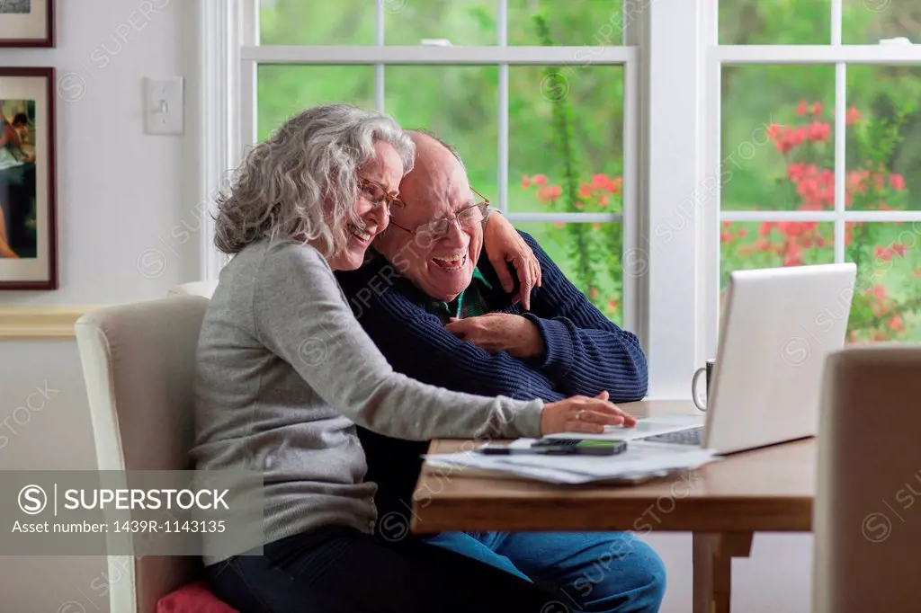Senior couple using laptop at home, laughing