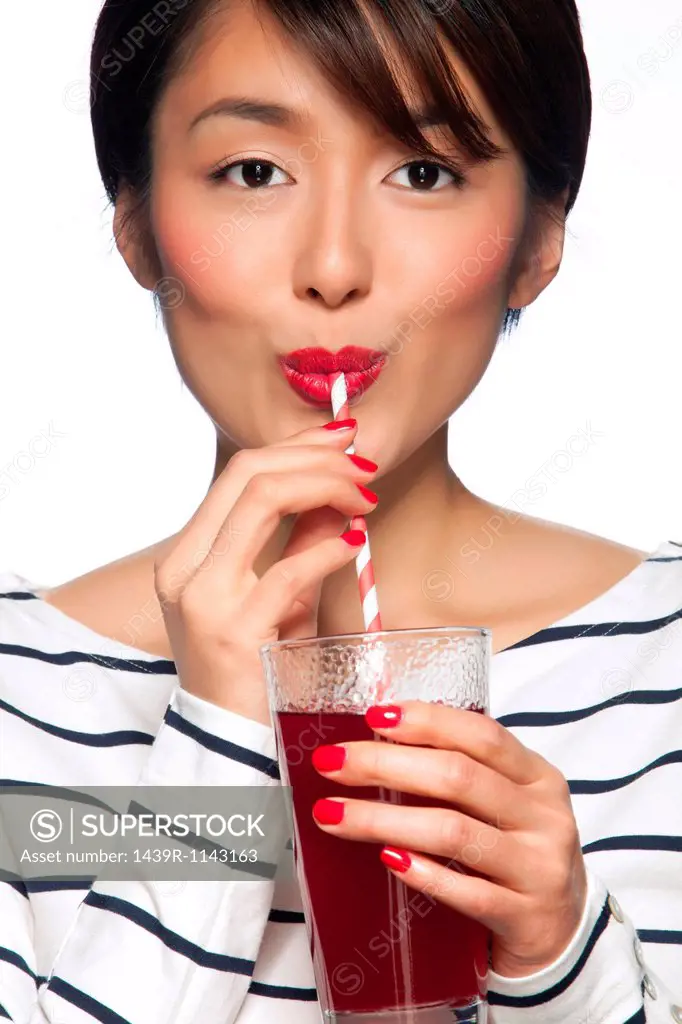 Young woman drinking from straw against white background