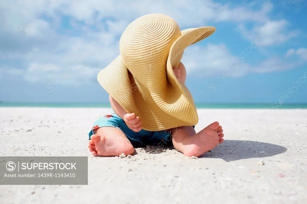 Baby boy playing with mother´s sun hat on the beach