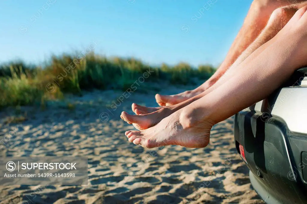 Mid adult couple sitting barefoot on car on beach