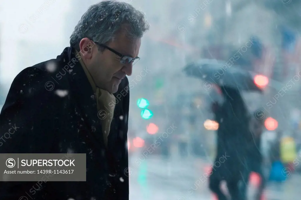 Mature man walking through snowstorm city