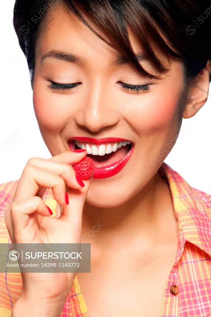 Young woman eating raspberry, studio shot