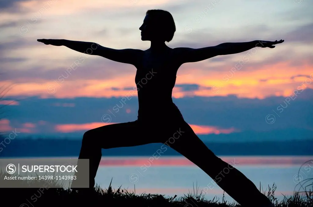 Silhouette of woman in warrior yoga pose at sunset