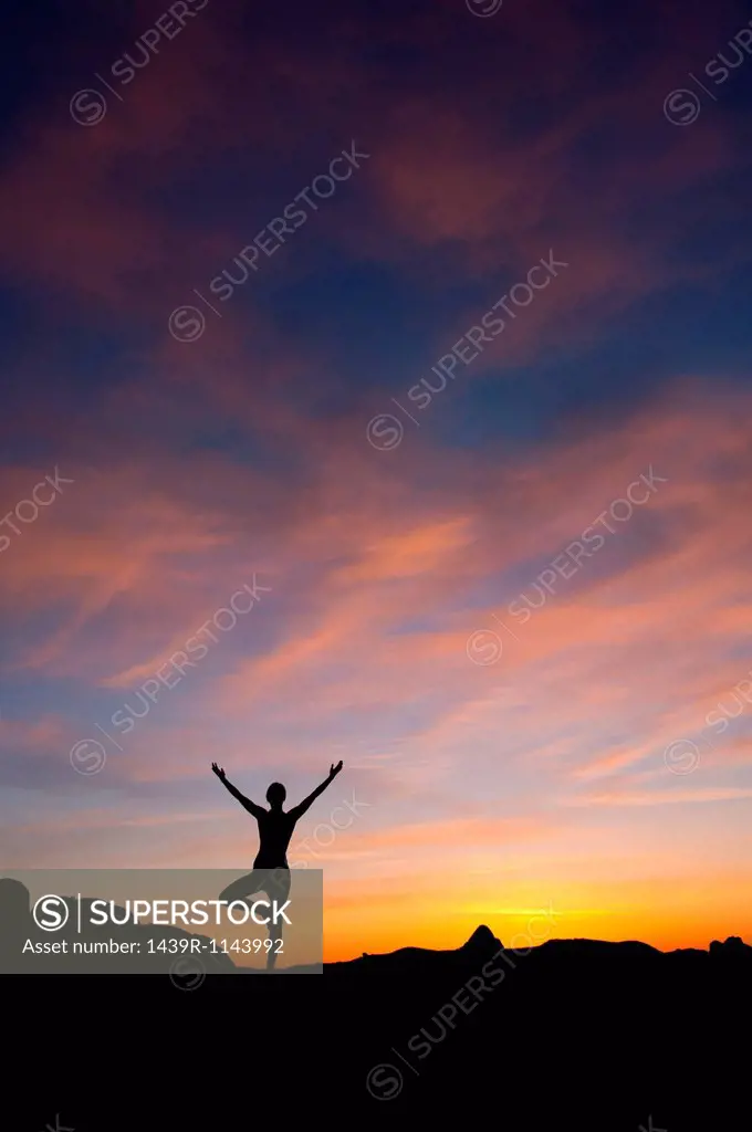 Young woman doing yoga in desert, silhouette