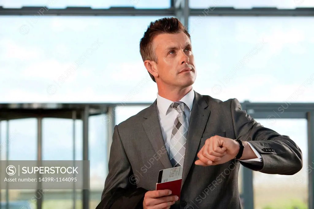 Businessman with airplane ticket and passport checking watch