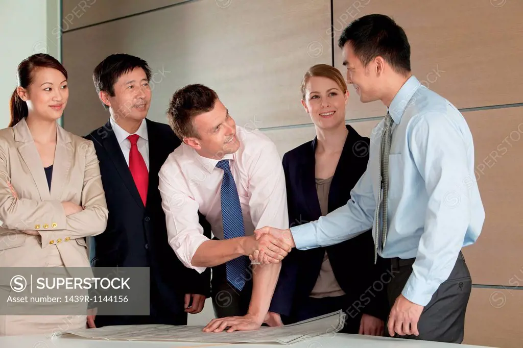 Multi racial businesspeople shaking hands over blueprint