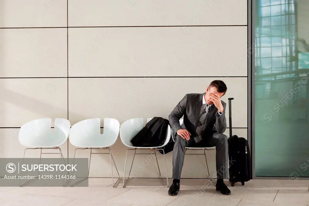 Businessman waiting with luggage and head in hands