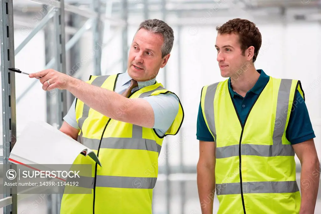 Two men in warehouse, one pointing with pen