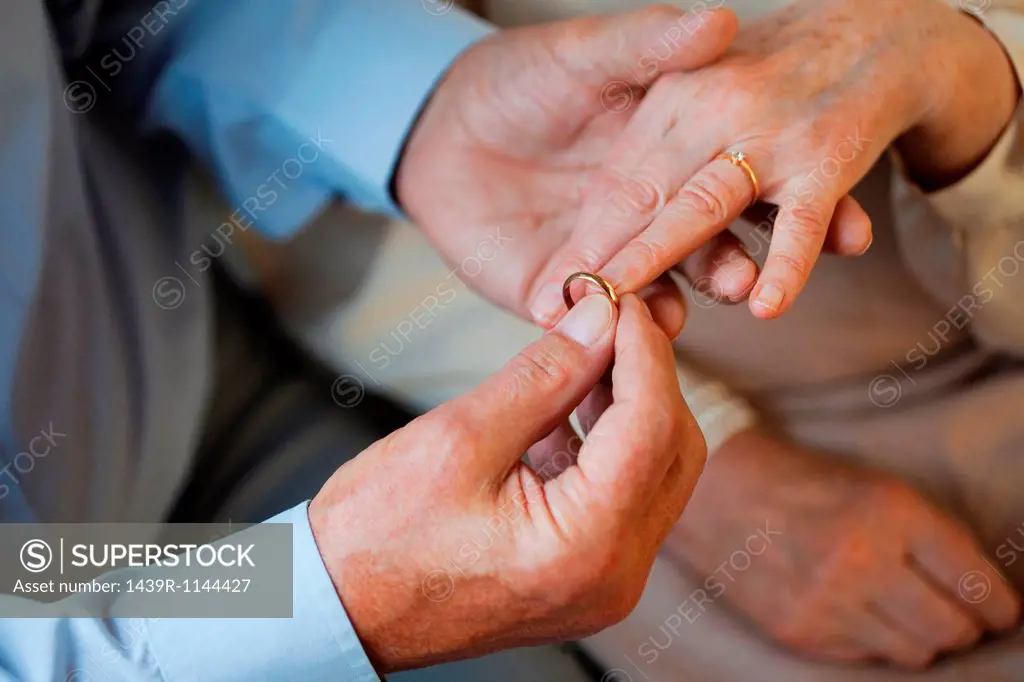 Senior man placing wedding ring on senior womans finger