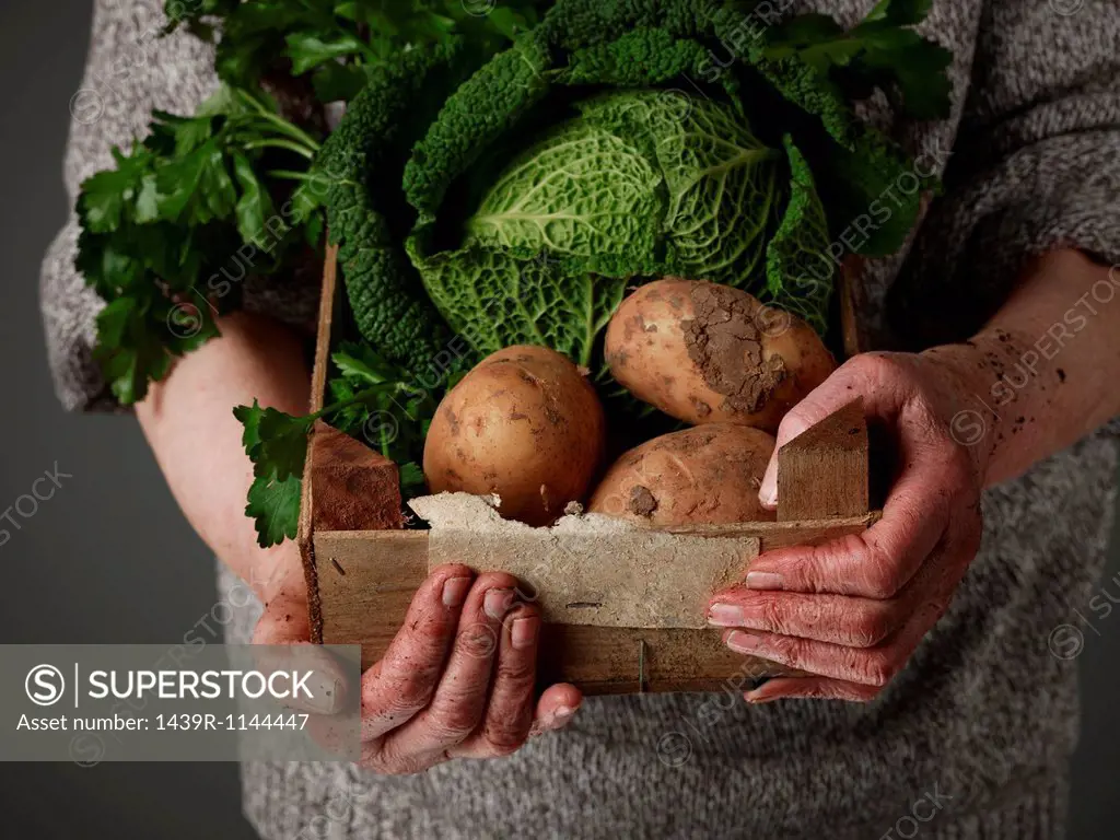 Woman holding wooden crate of vegetables