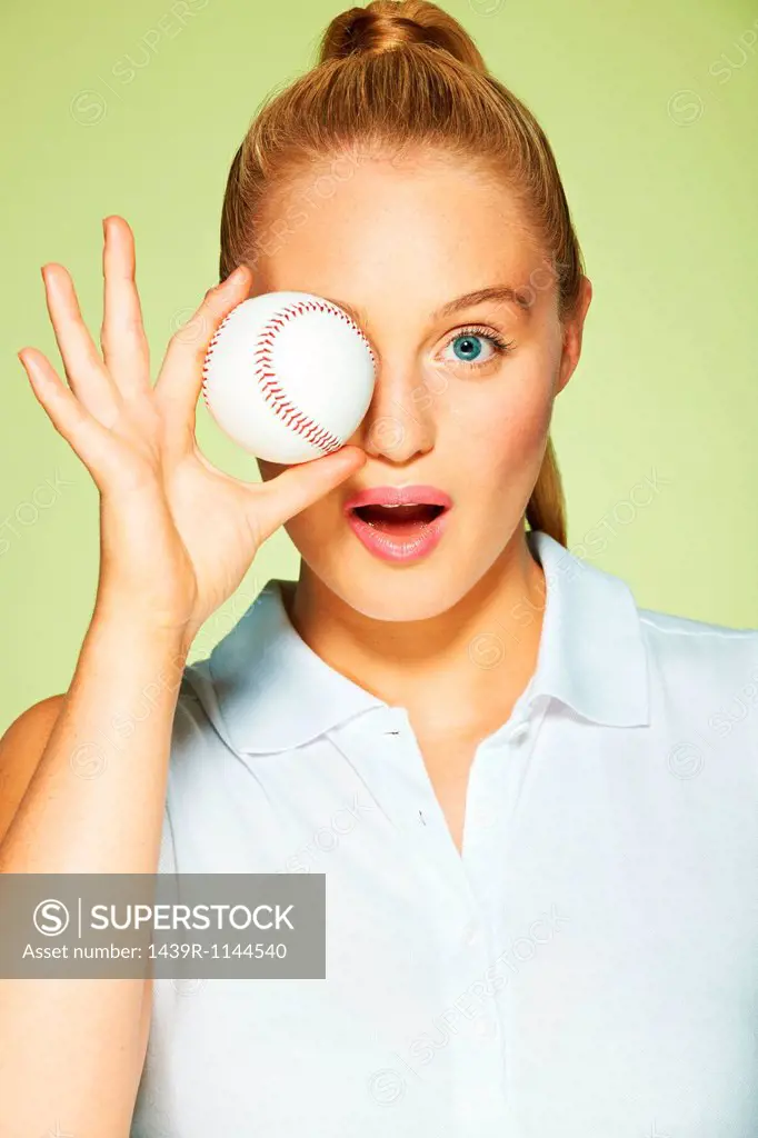 Young woman holding baseball in front of eye