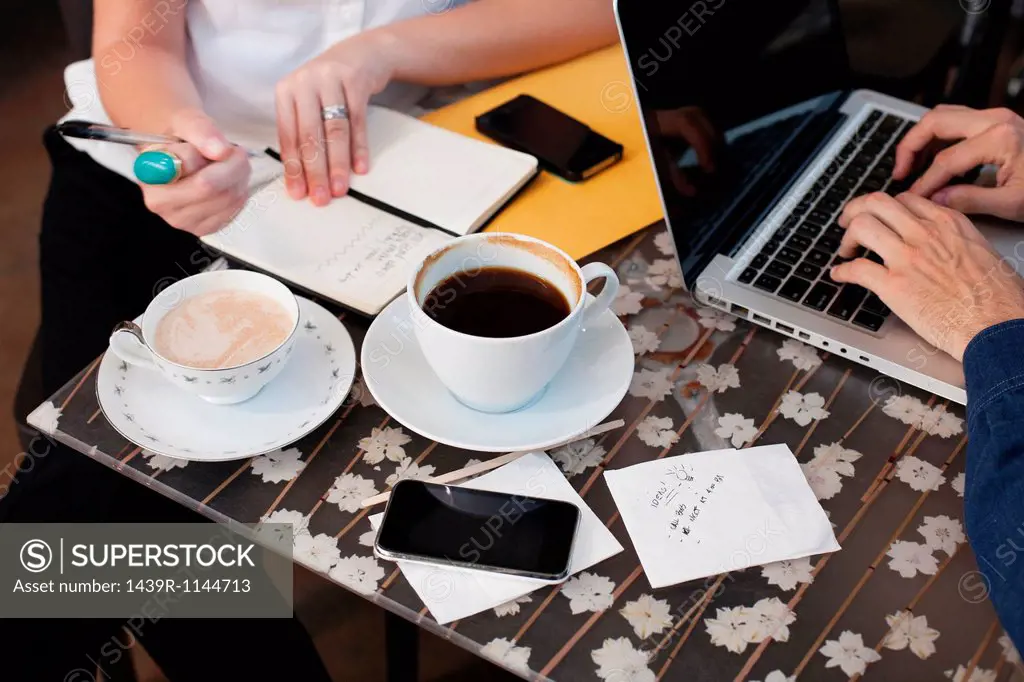 Businesspeople in cafe, man using laptop woman writing