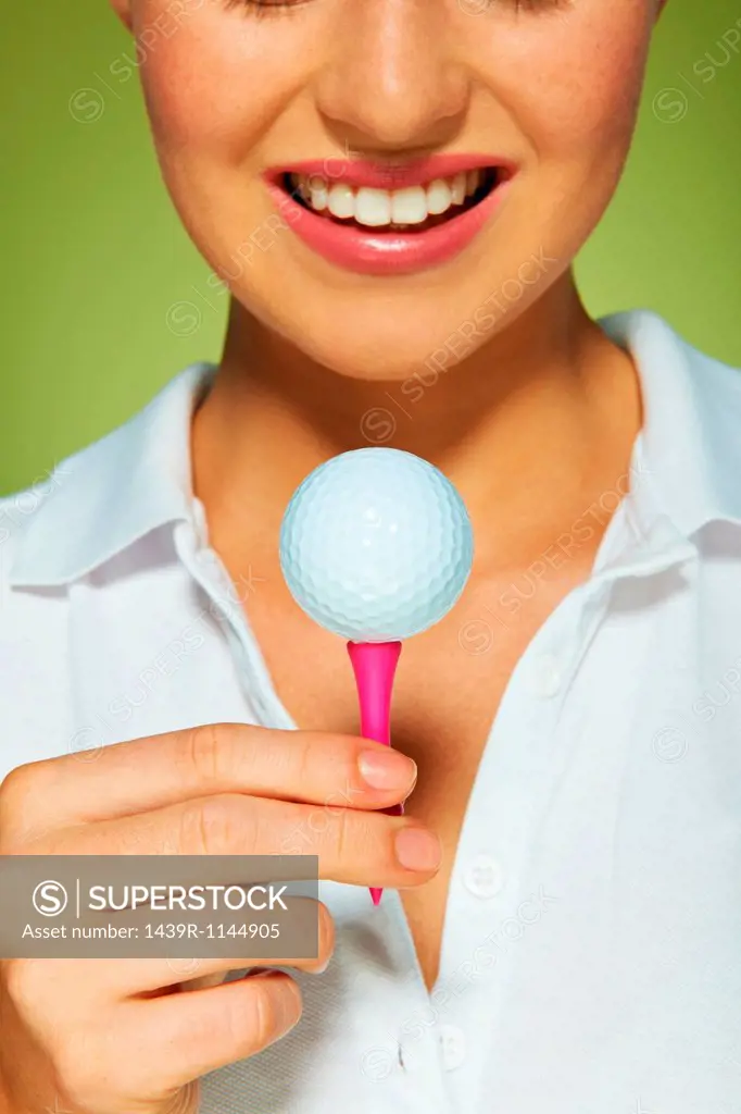 Young woman holding golf ball and tee
