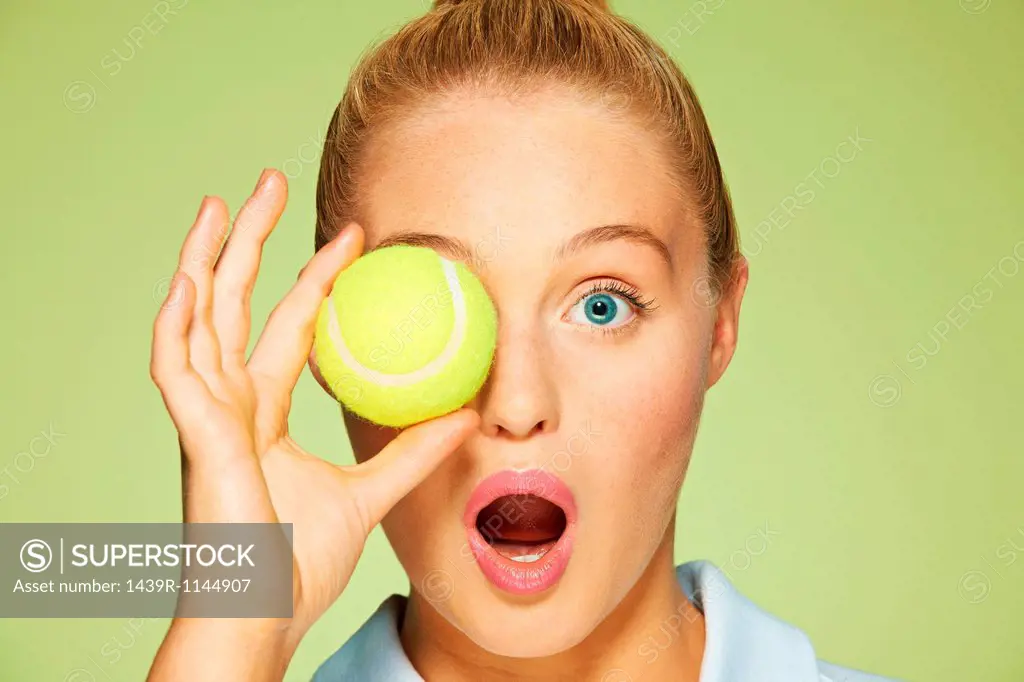 Young woman holding tennis ball over her eye