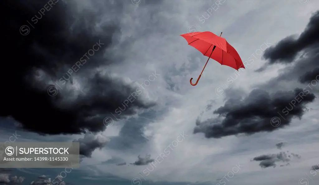 Red umbrella floating through cloudy sky
