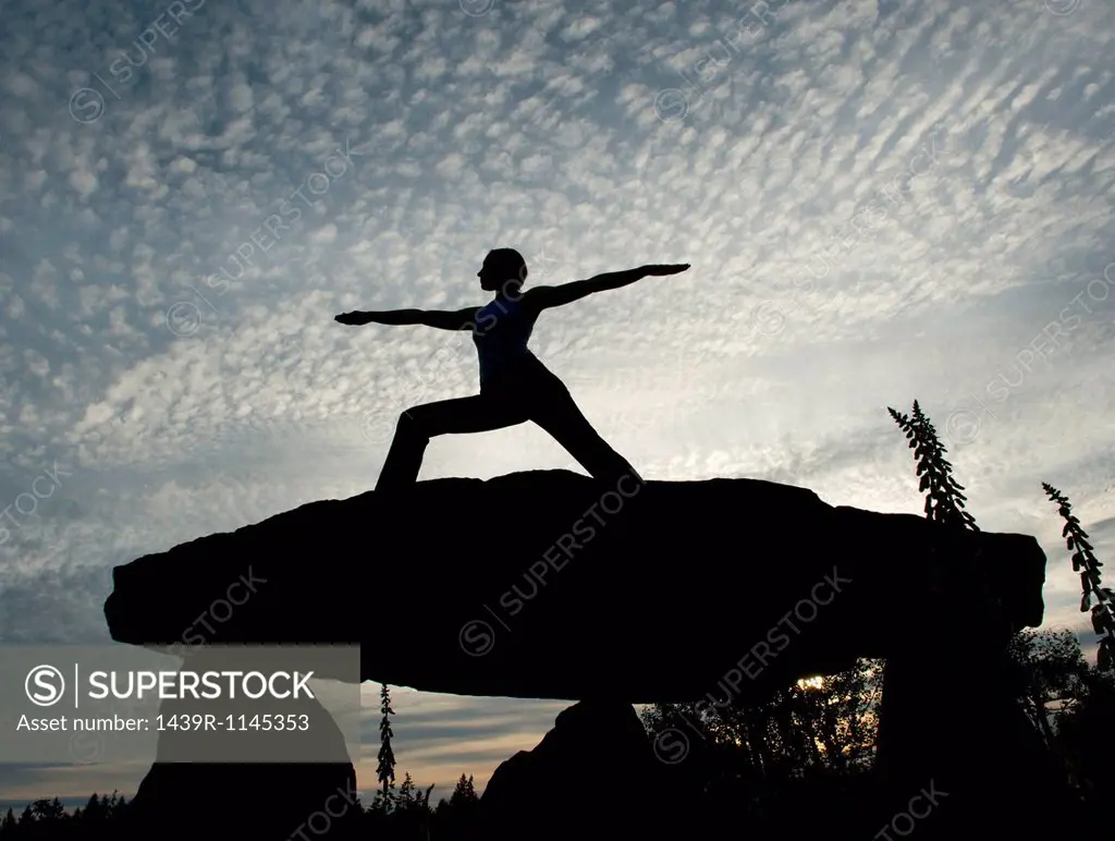 Silhouette of woman in warrior yoga pose on a rock