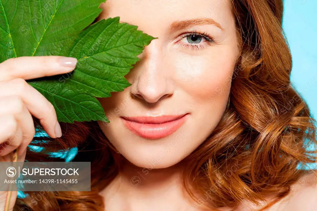 Woman covering eye with green leaf