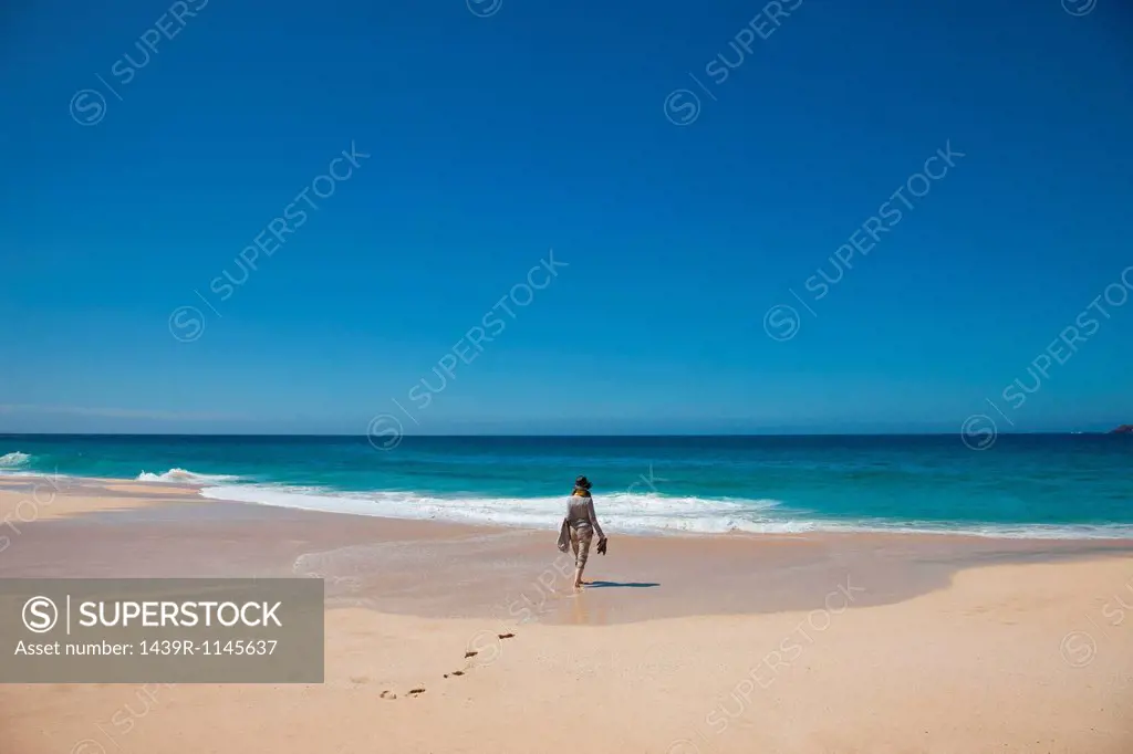 Woman alone on a beach, walking toward the sea