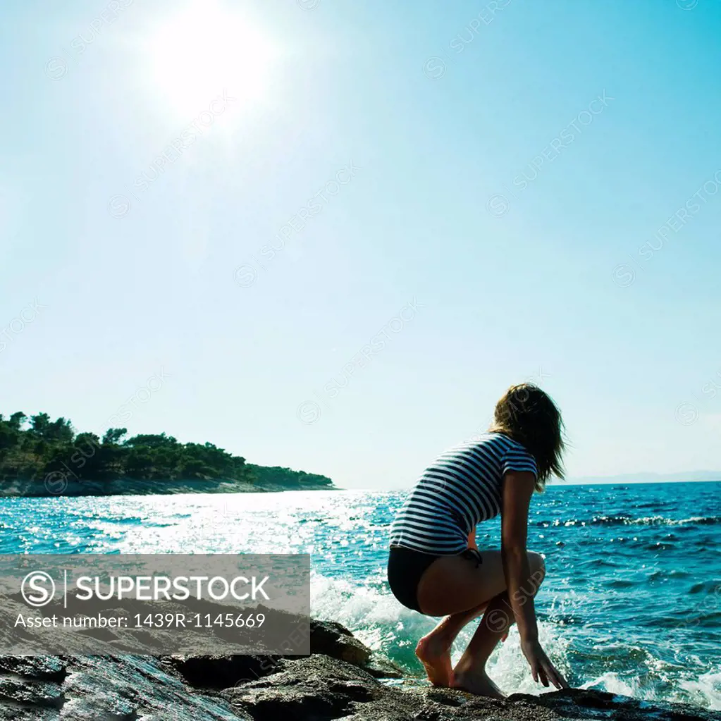 Young woman crouching by the sea