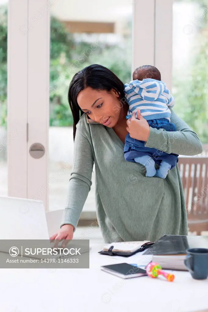 Young woman holding baby and using laptop