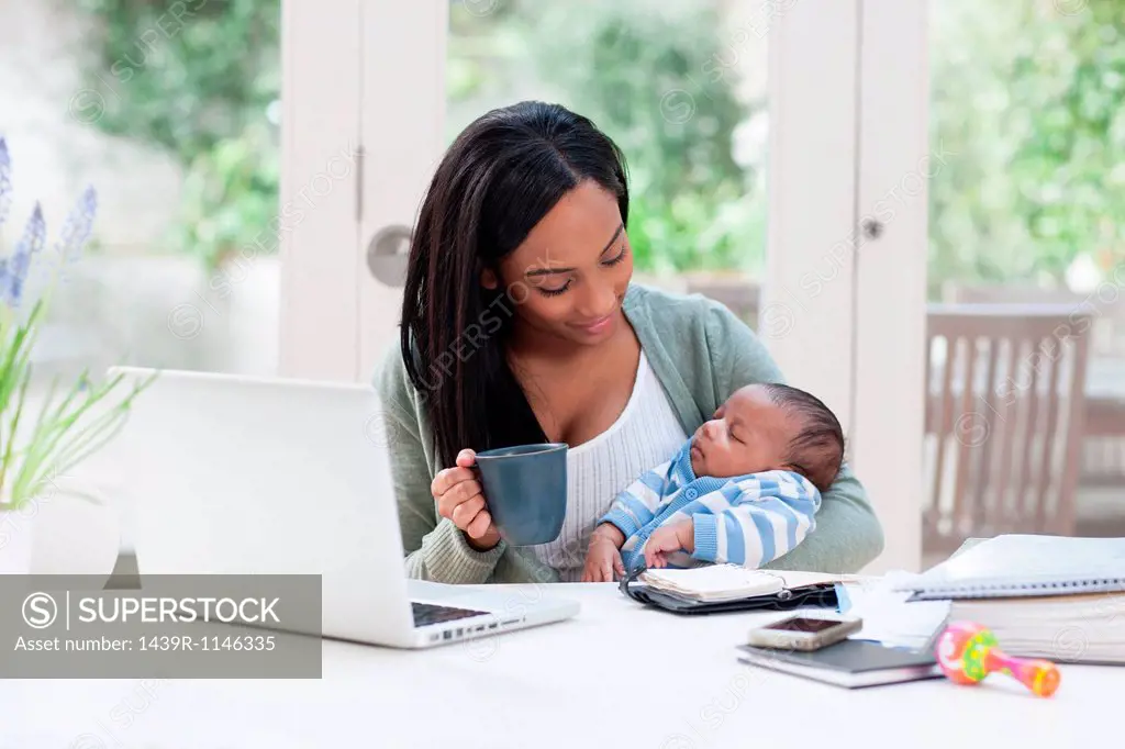 Mother holding baby son, with laptop and coffee cup