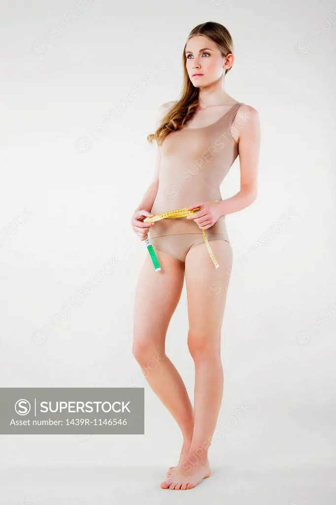 Young woman measuring waist with tape measure