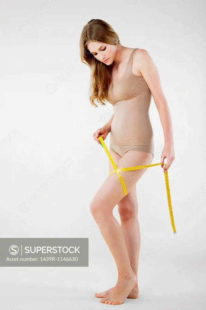 Young woman measuring thigh with tape measure