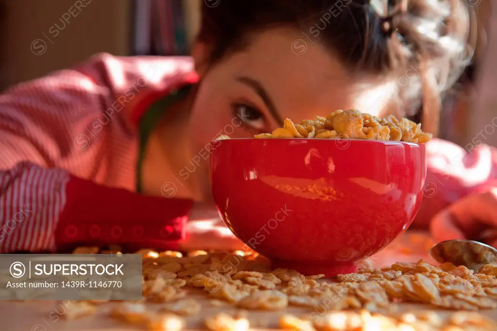 Young woman looking out from behind bowl and spilt breakfast cereal