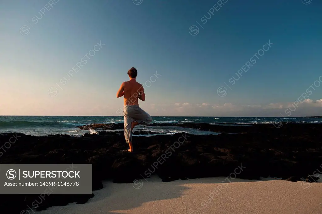 Man with bare chest performing yoga pose on Lava flow by the ocean on the Big Island of Hawaii