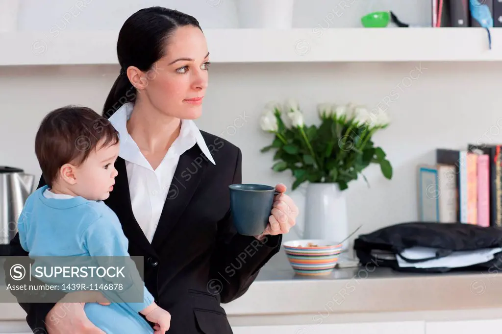 Businesswoman holding baby son and coffee cup