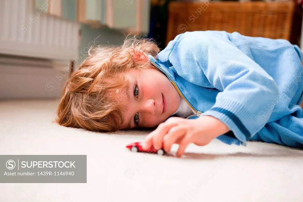 Young boy lying on his side playing with a toy car