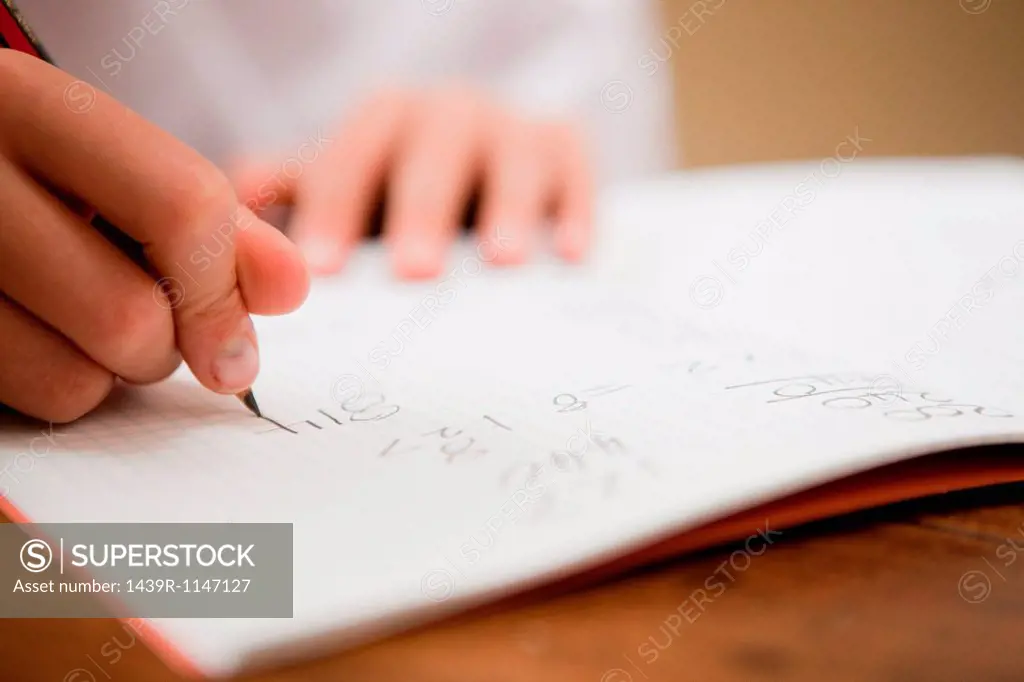 Close up of the hands of a young boy writing in a textbook