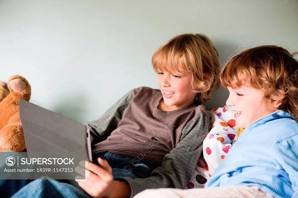 Two young boys on a bed, using a digital tablet