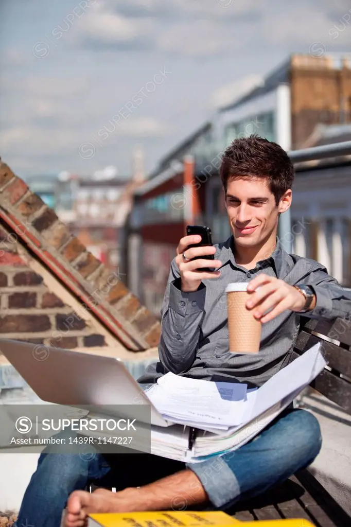 Young man sitting in a roof garden with laptop and mobile phone