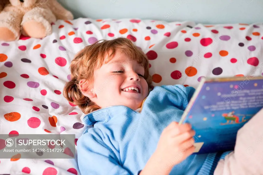 Young boy reading a book on his bed