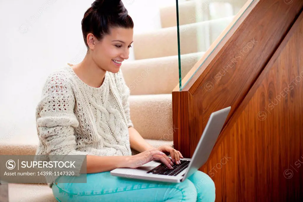 Young woman sitting on stairs using laptop