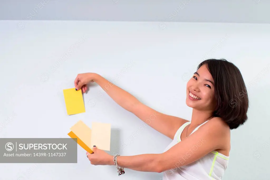 Young woman holding up color swatches to wall