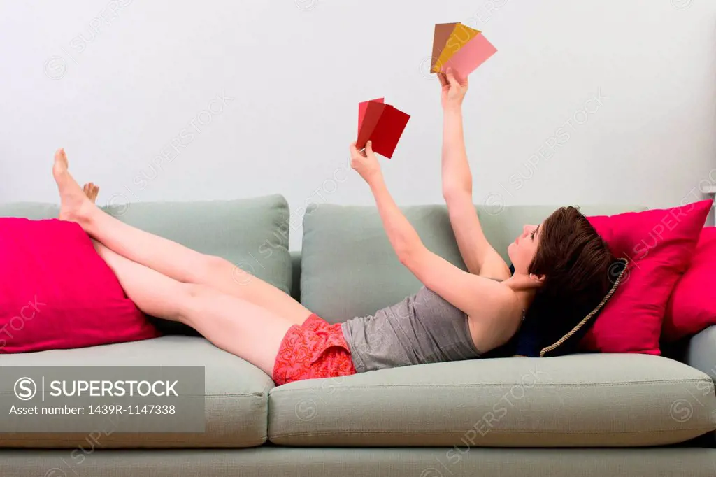 Young woman lying on sofa, looking at color swatches