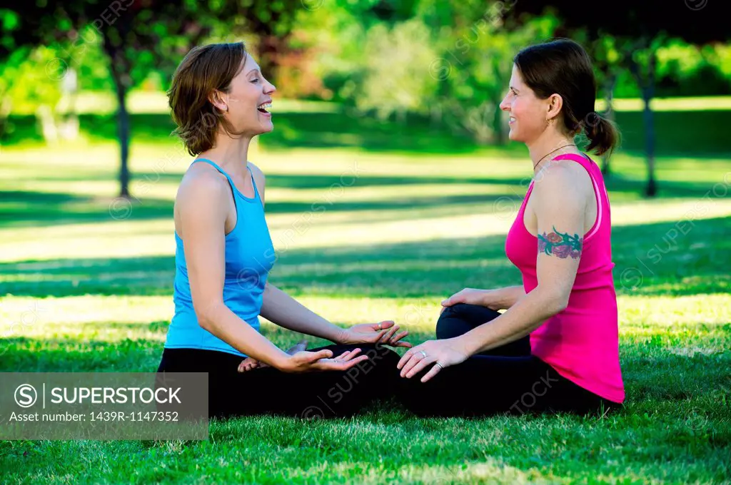 Women practising yoga in park, sitting face to face