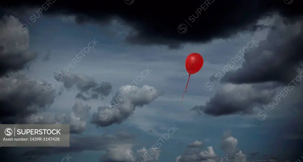 Red balloon floating through dark sky