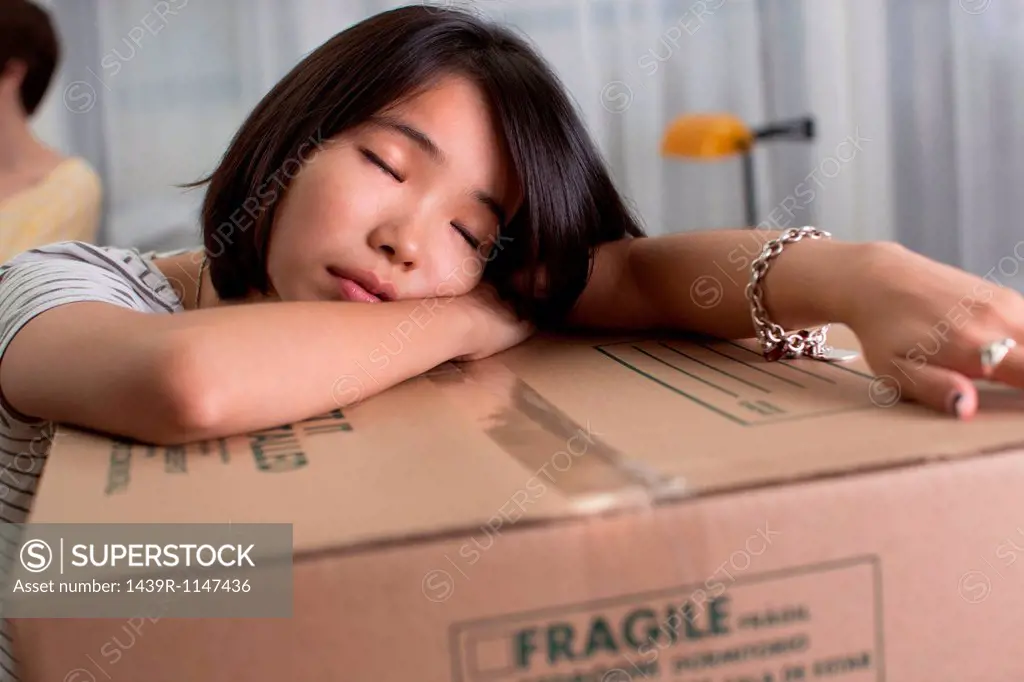 Tired young woman resting on moving box