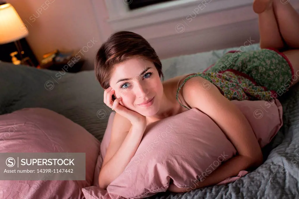 Young woman lying on her bed, holding pillow