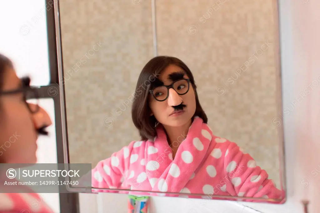 Young woman looking herself wearing funny disguise